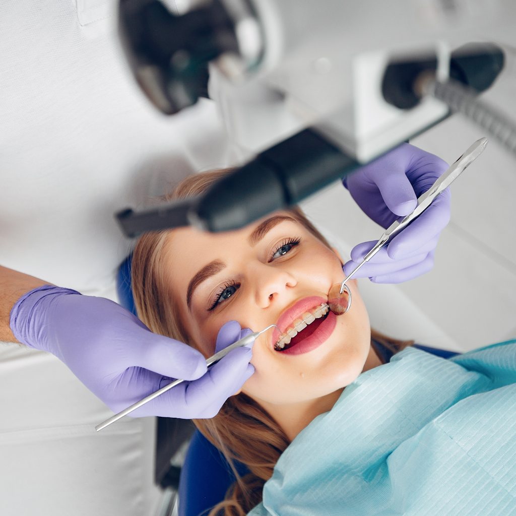 A smiling patient with braces in a dental chair is examined by a dentist wearing purple gloves, holding dental tools. The setting feels calm and professional.