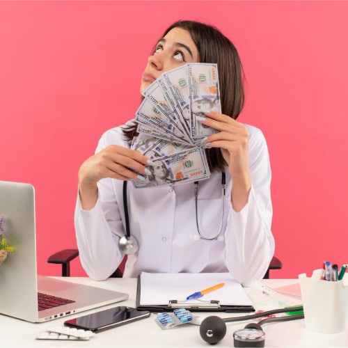 A doctor in a white coat holds a fan of dollar bills, looking upwards thoughtfully. The office desk is cluttered with medical tools, a laptop, and papers, set against a pink background.