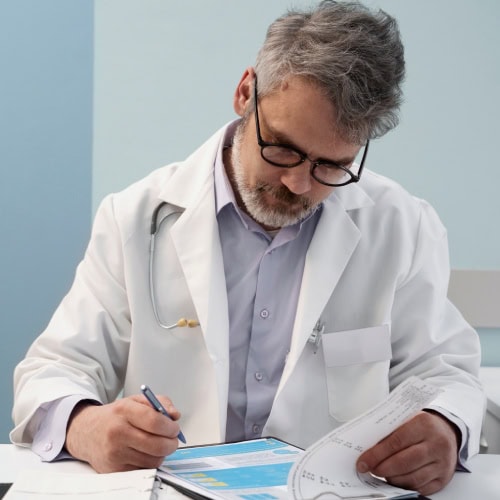 A doctor in a white coat and glasses writes on a clipboard, focusing intently. A stethoscope hangs over his shoulder. The setting is a calm, professional office.