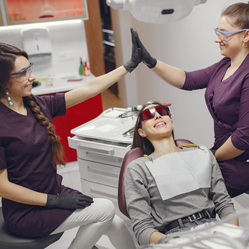 Two dental professionals high-five near a smiling patient sitting in a dental chair, conveying positivity and teamwork in a clinical setting.