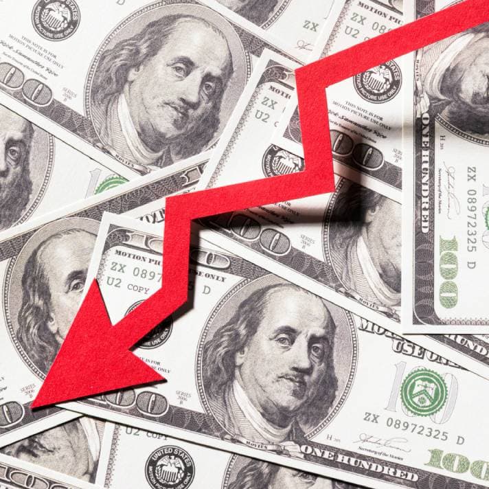 Red downward arrow on a background of U.S. one hundred dollar bills, symbolizing economic decline or financial downturn.
